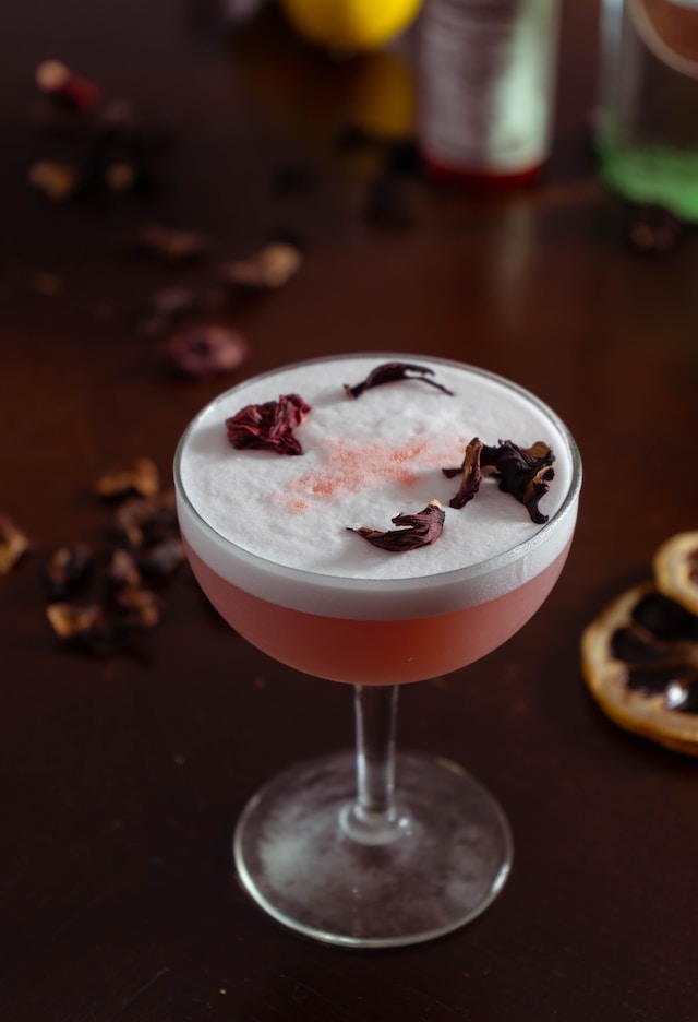 A pink craft cocktail with floral garnish