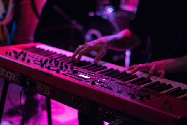 A person playing the keyboard in a dueling piano bar with pink neon lighting.