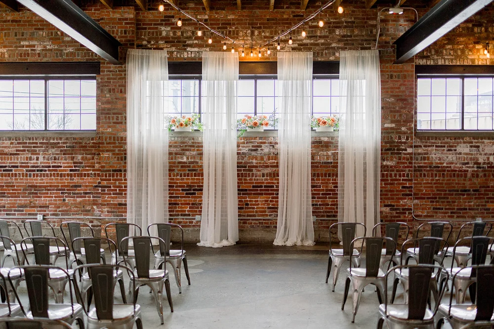 Wedding ceremony with four panels of draping and flowers in the window at INDUSTRY in Indianapolis, IN