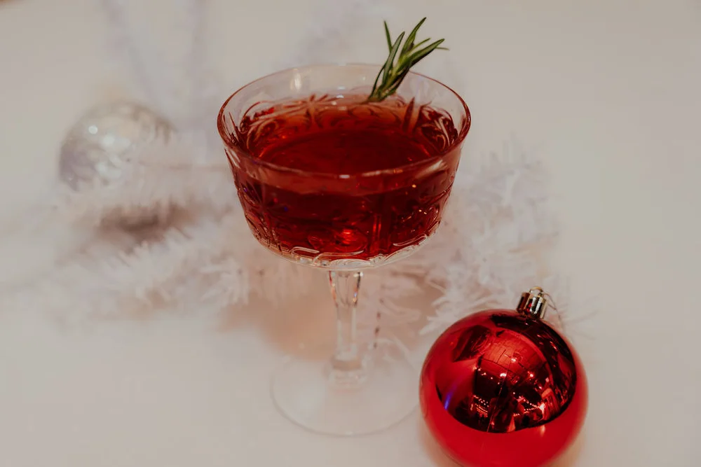 Red cocktail in a vintage glass with mint garnish and red ornament at Indy holiday party