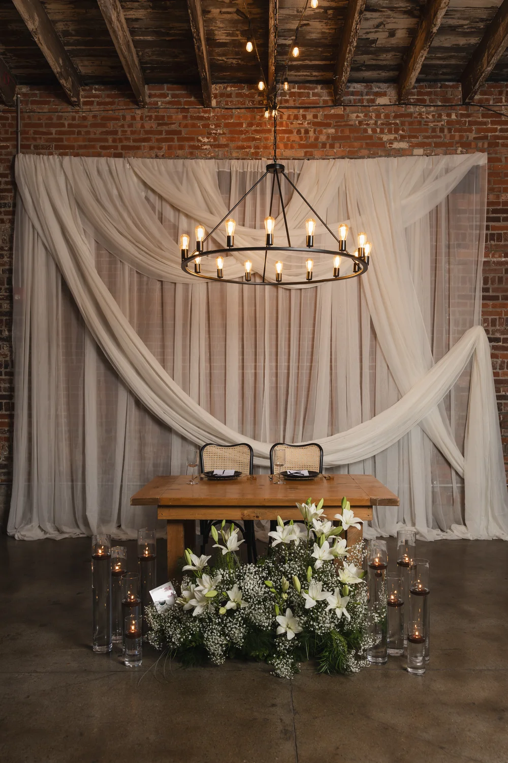 Sweetheart table with wicker chairs, chandelier, and white draping at INDUSTRY Indianapolis wedding venue